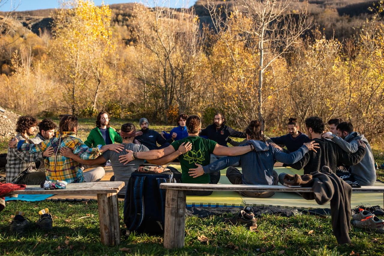 A group sitting together outdoors, seen from a distance against a mountain backdrop