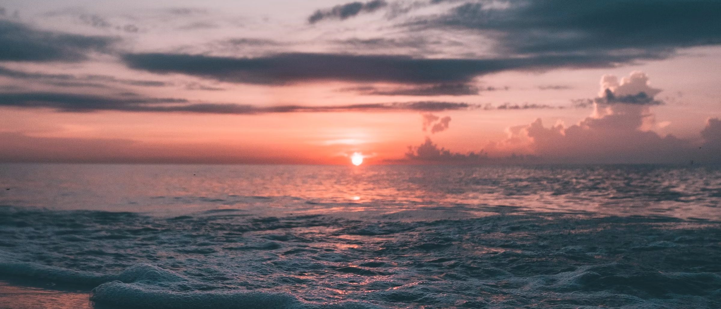 An empty sandy shoreline at first light, calm grey-blue water meeting the horizon